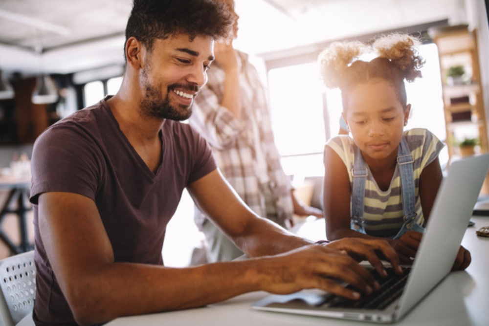 Parent working on a laptop with a child looking on.